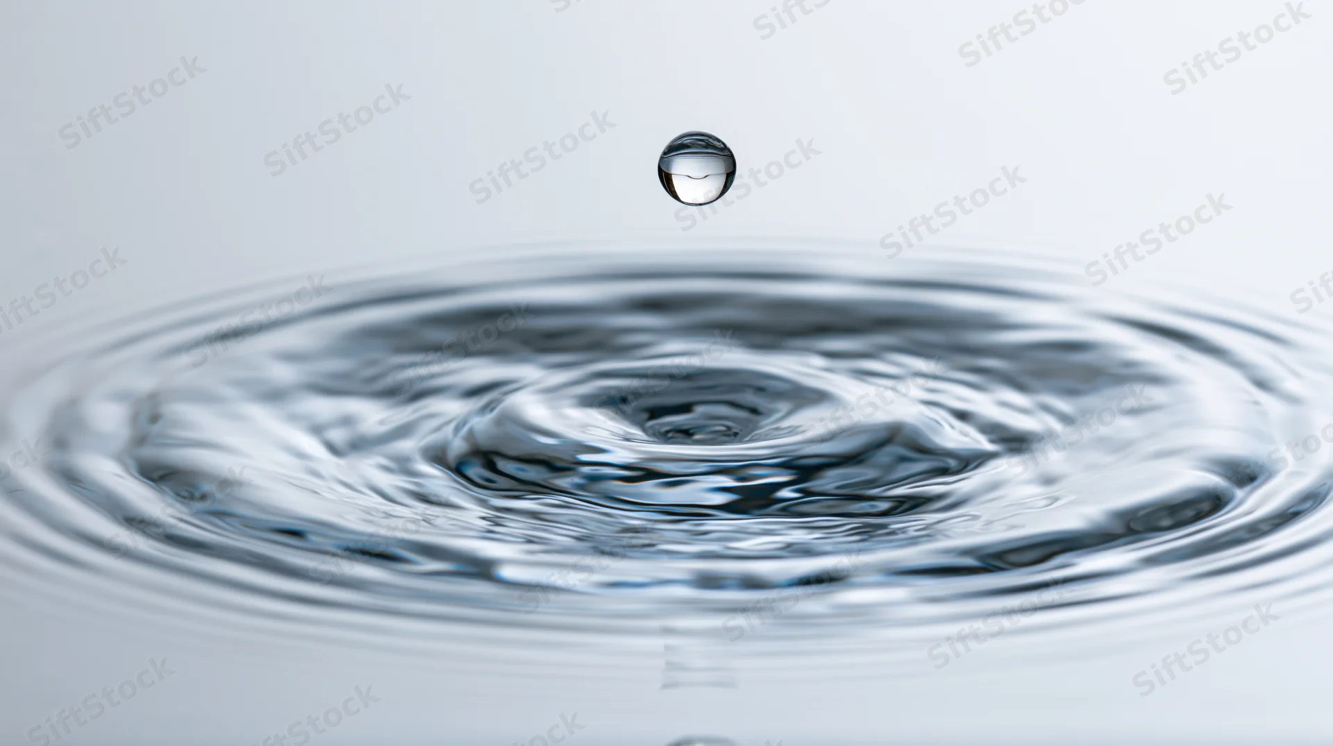Single water droplet suspended above rippling surface in studio setting