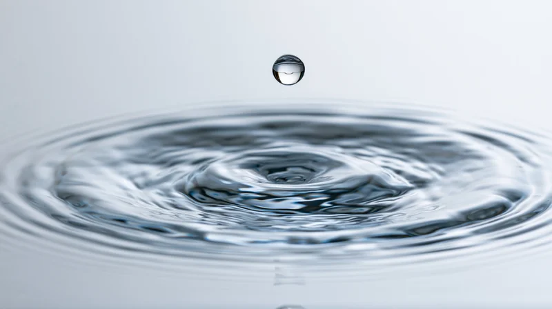 Single water droplet suspended above rippling surface in studio setting