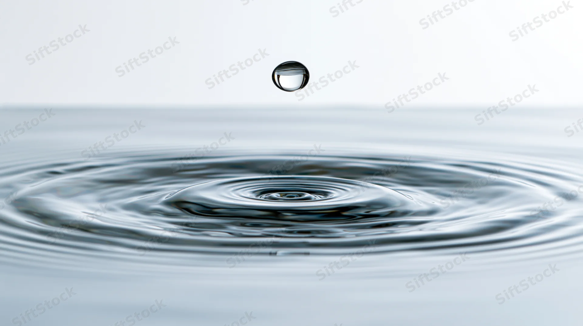 Water droplet suspended above rippling surface creating concentric waves