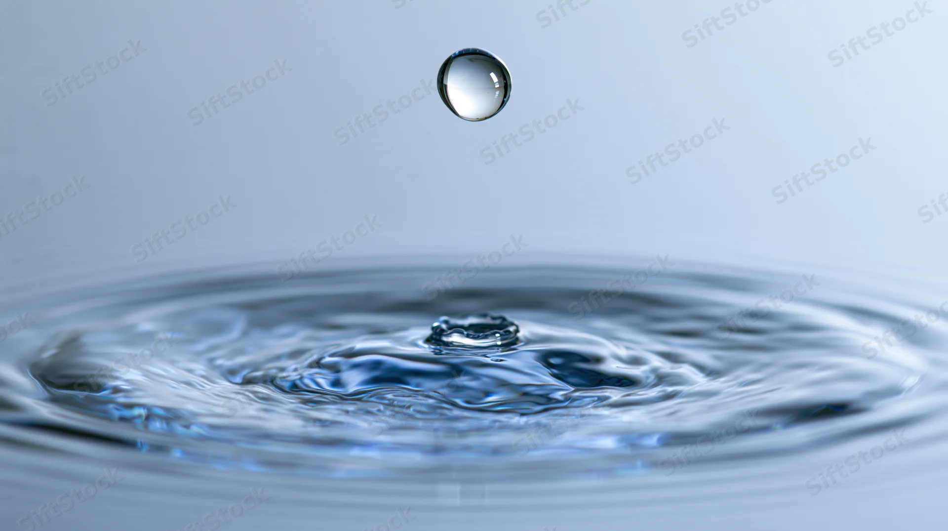 Single water droplet suspended above rippling surface in studio setting