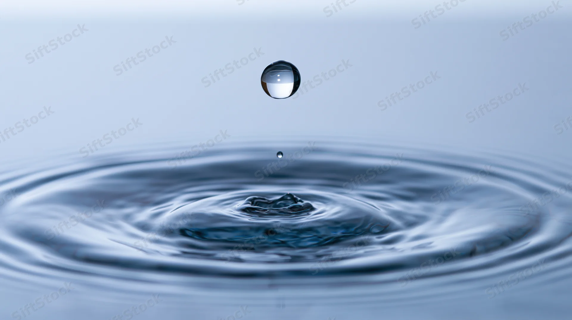 Water droplet suspended midair above rippling surface creating concentric ripples
