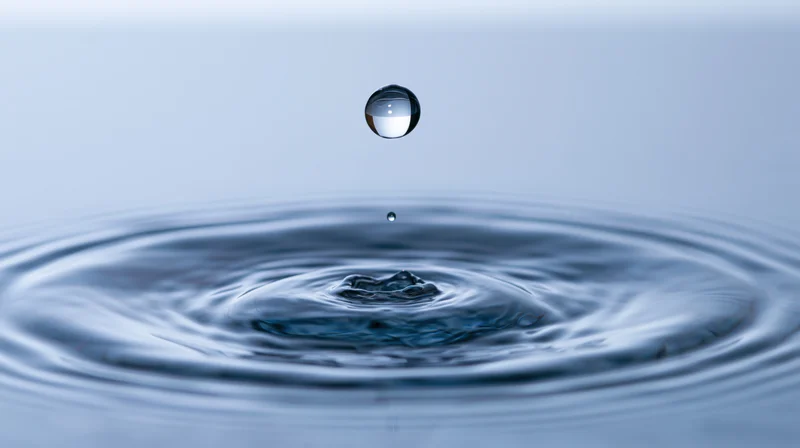 Water droplet suspended midair above rippling surface creating concentric ripples