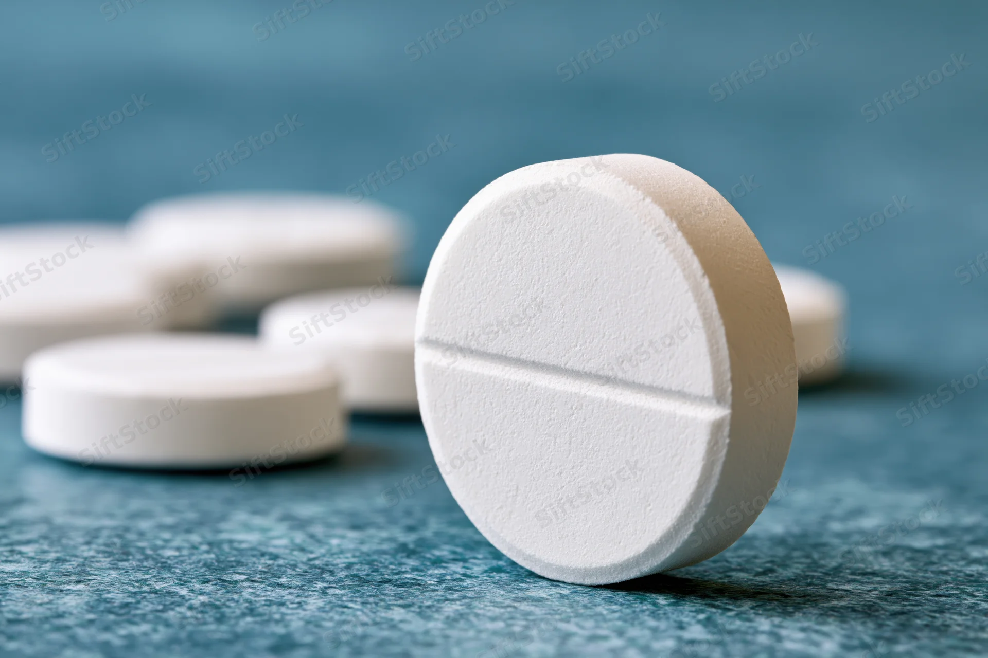 White round scored tablet standing upright on textured blue surface with other tablets blurred in background