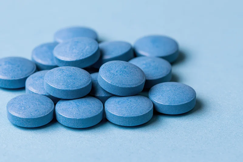 Blue pharmaceutical tablets scattered on a light blue surface