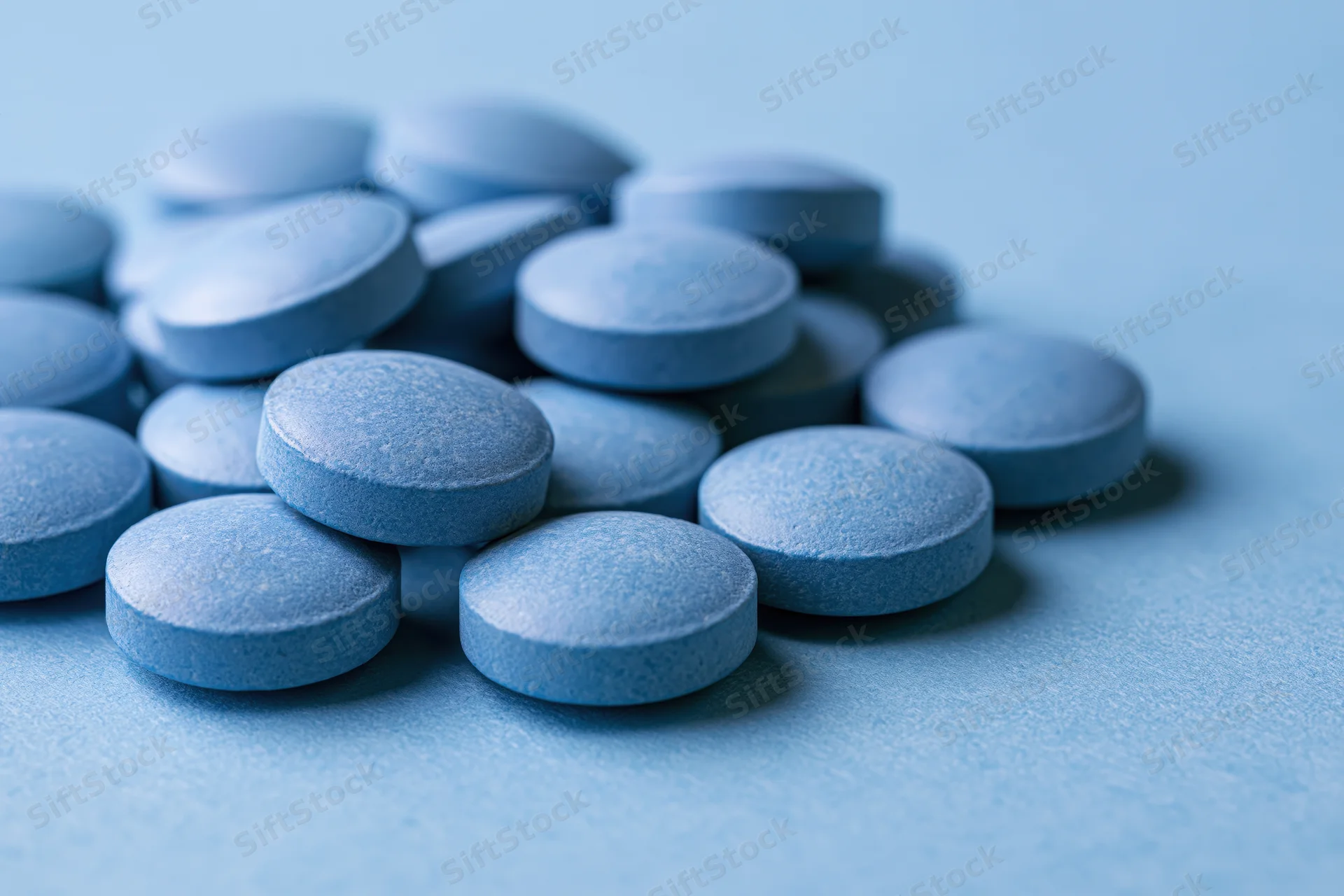 Blue pharmaceutical tablets scattered on a light blue surface