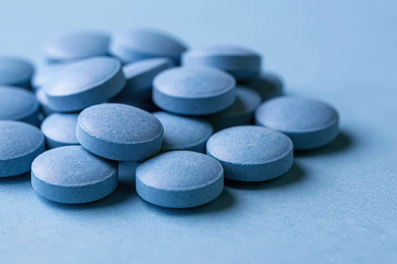 Blue pharmaceutical tablets scattered on a light blue surface
