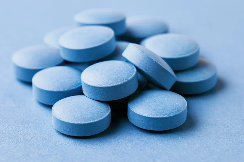 Blue pharmaceutical tablets scattered on a plain surface