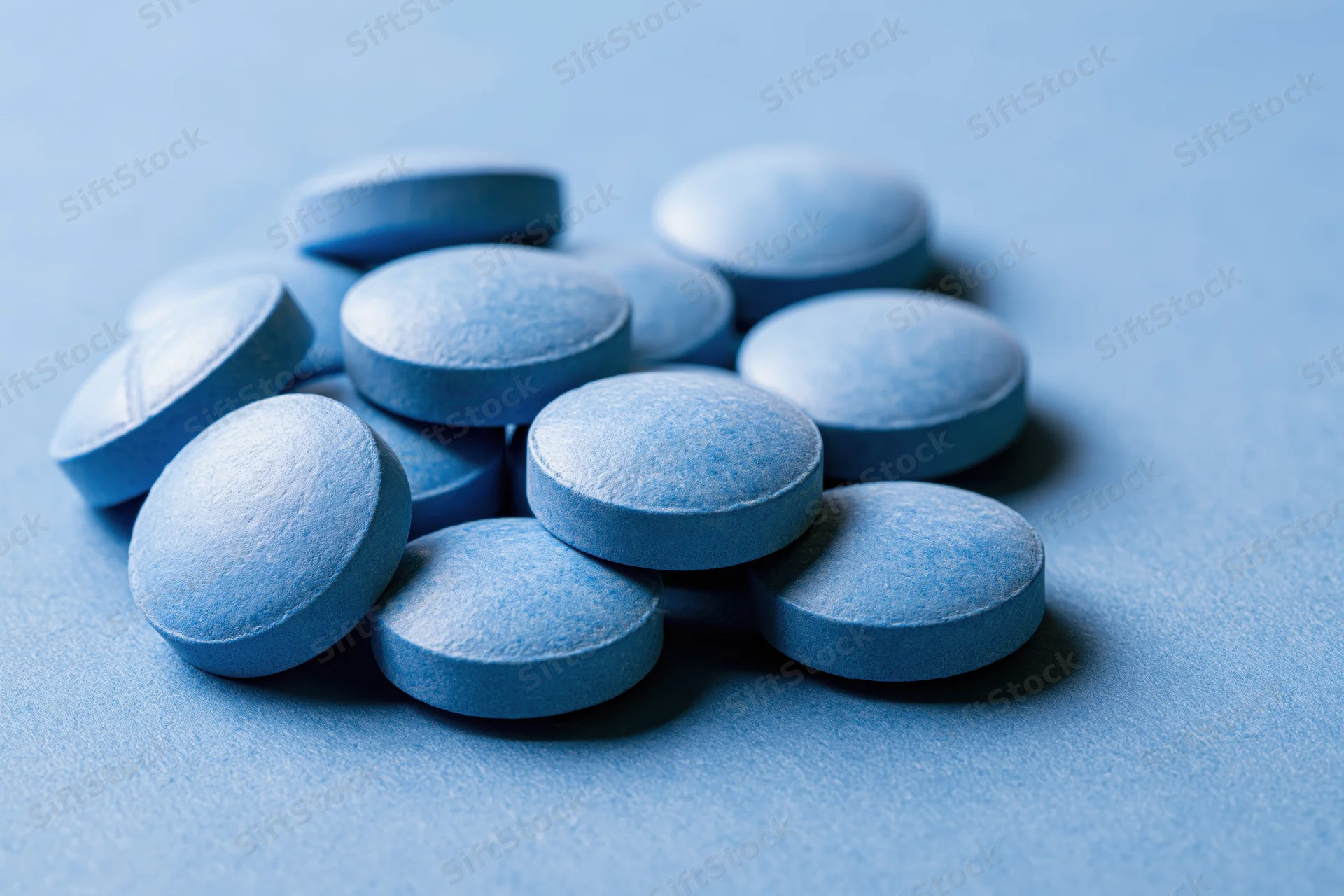 Blue pharmaceutical tablets scattered on a blue surface
