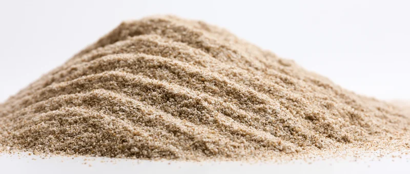 A mound of fine dry sand with rippled ridges on a white surface