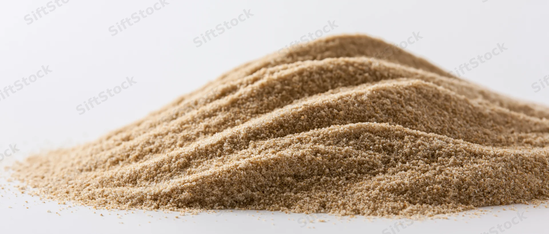 A small elongated pile of fine dry sand with soft rippled ridges on a white surface