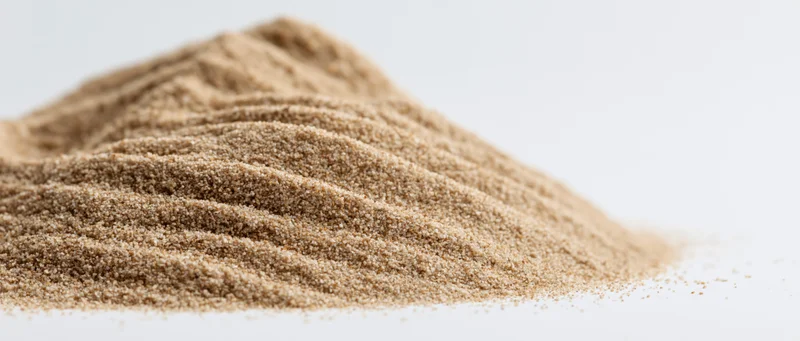A small elongated pile of fine dry sand with soft rippled ridges on a white surface
