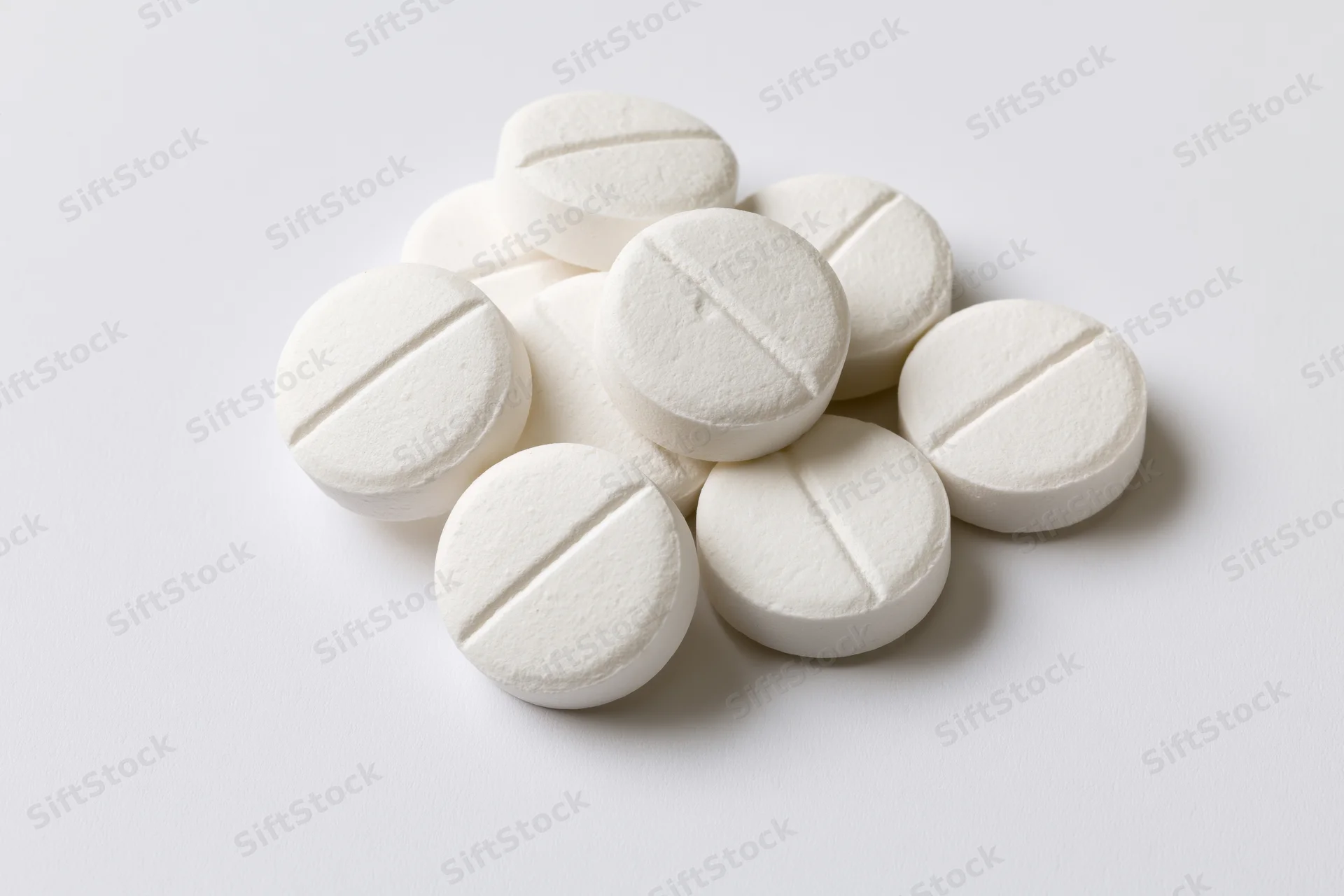 Round white pharmaceutical tablets piled loosely on a white surface