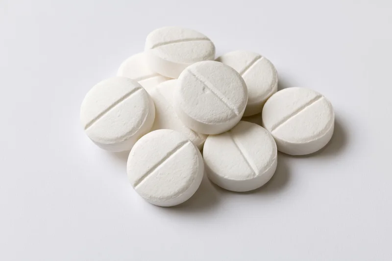 Round white pharmaceutical tablets piled loosely on a white surface