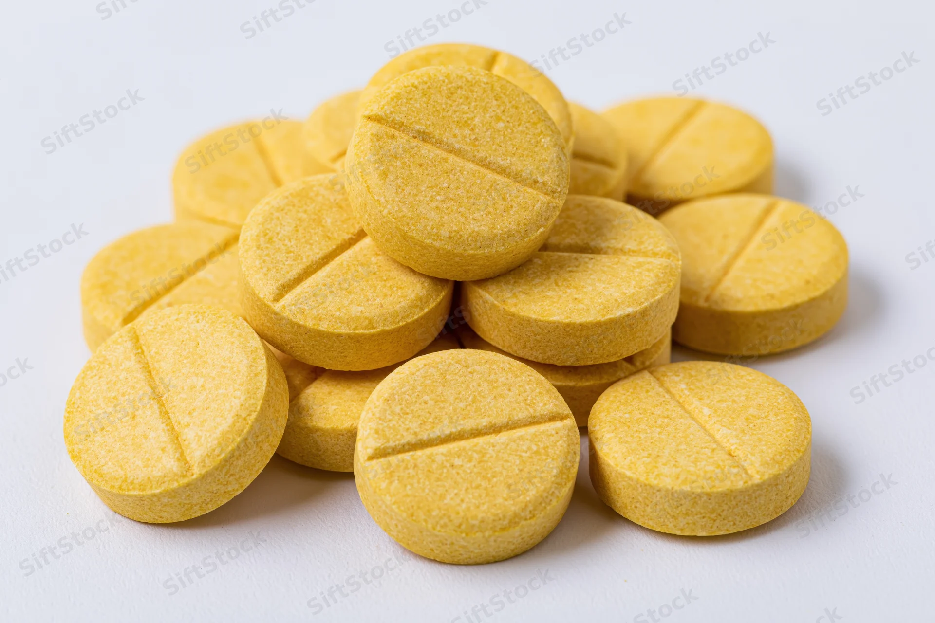 A pile of round yellow scored tablets stacked loosely on a white surface