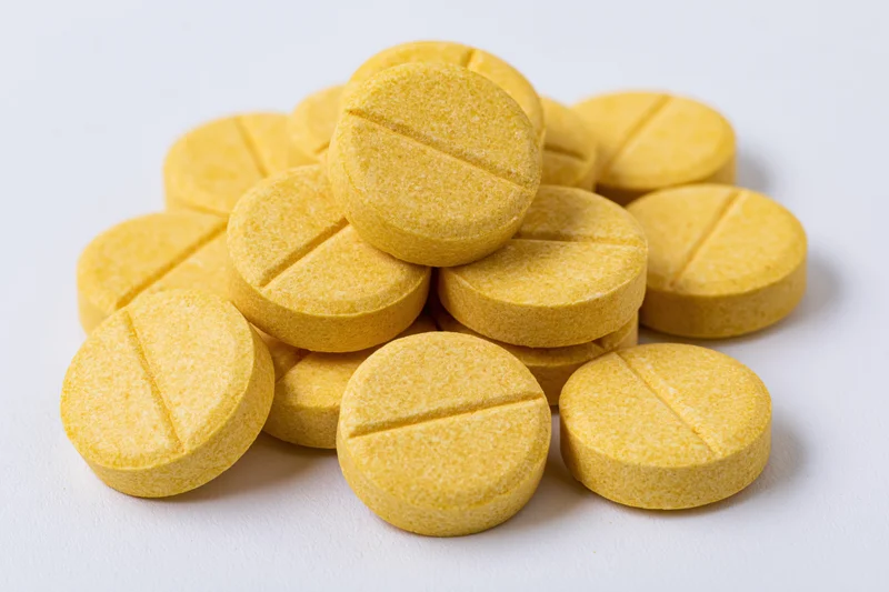 A pile of round yellow scored tablets stacked loosely on a white surface