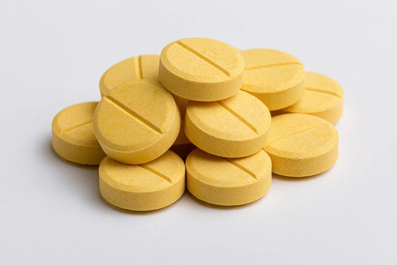 A pile of round yellow scored tablets stacked on a white surface