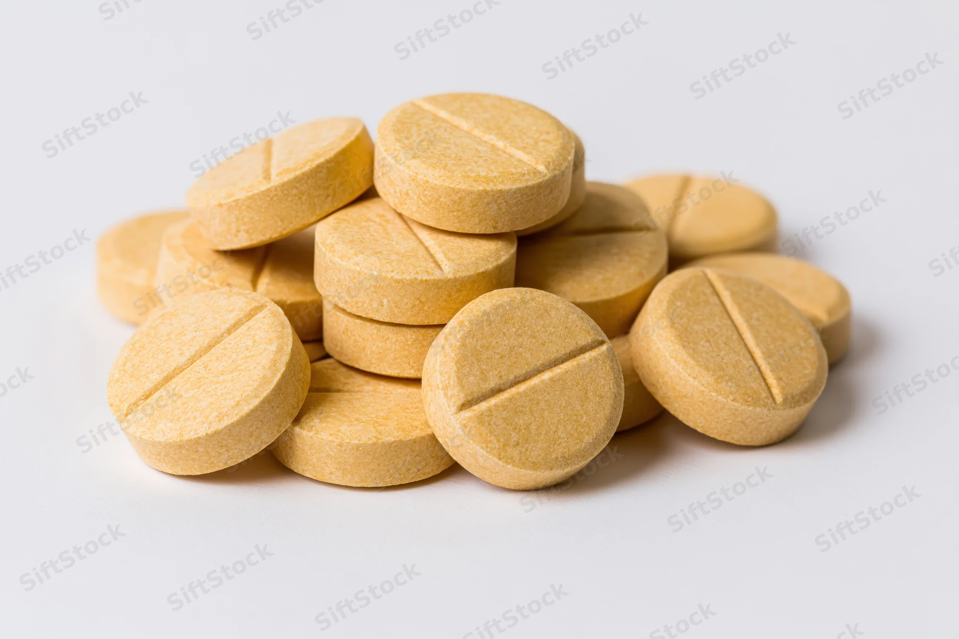 A pile of round yellow scored tablets on a white background