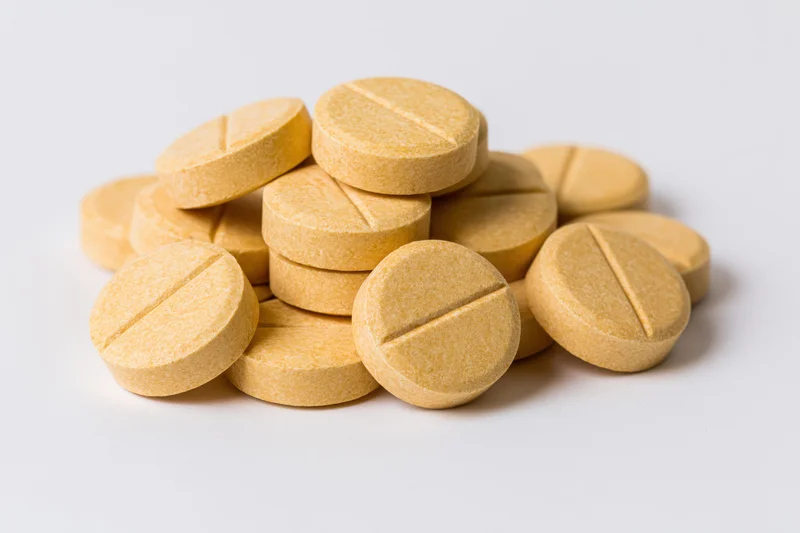 A pile of round yellow scored tablets on a white background
