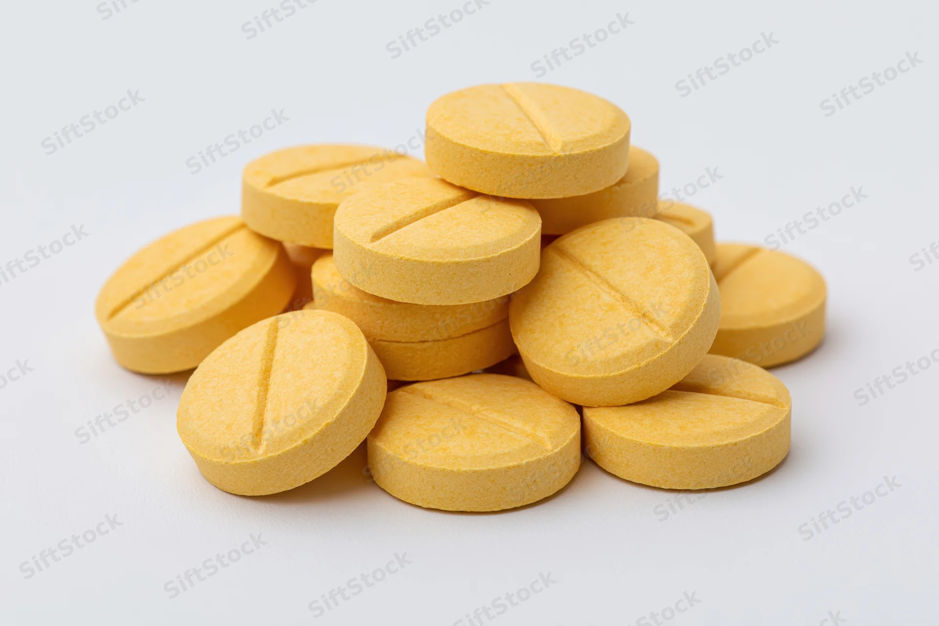 A pile of round yellow scored tablets stacked loosely on a white surface