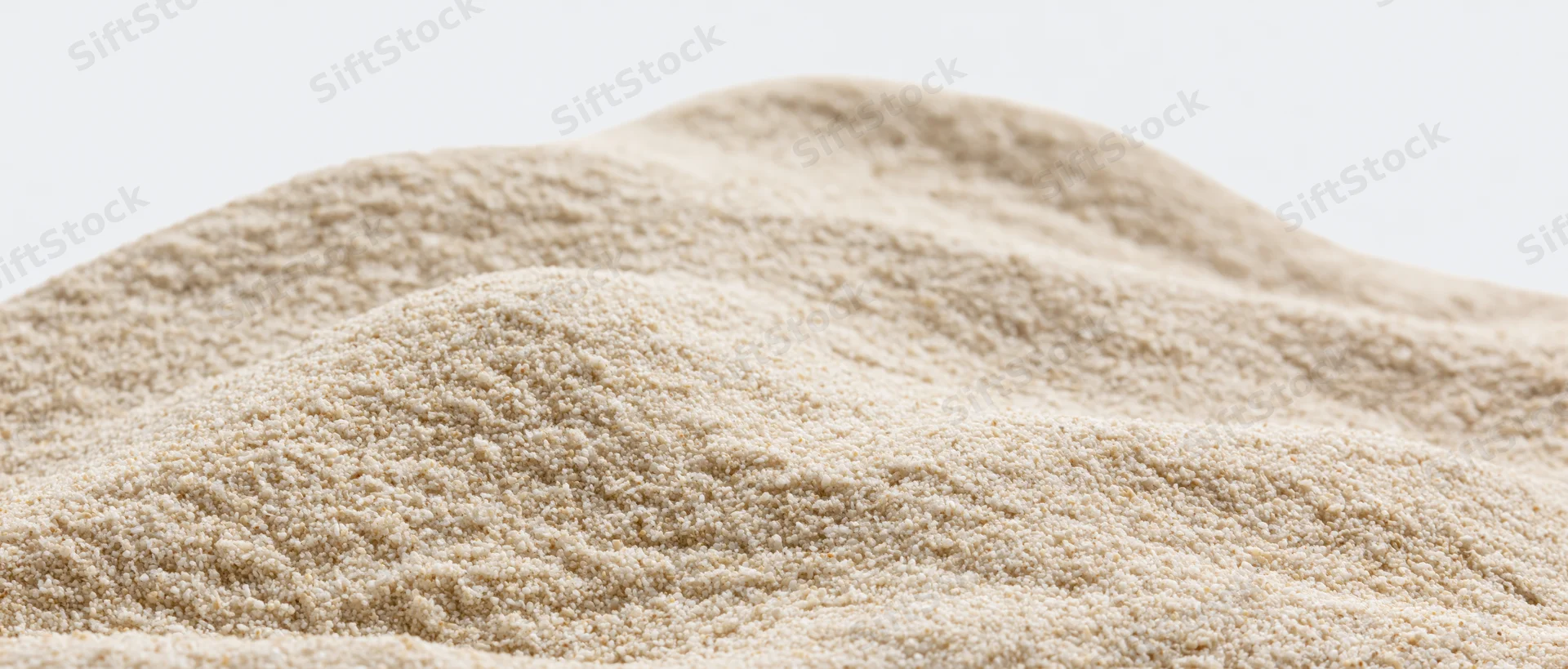 Closeup of a mound of dry beach sand with gently undulating surface against white background