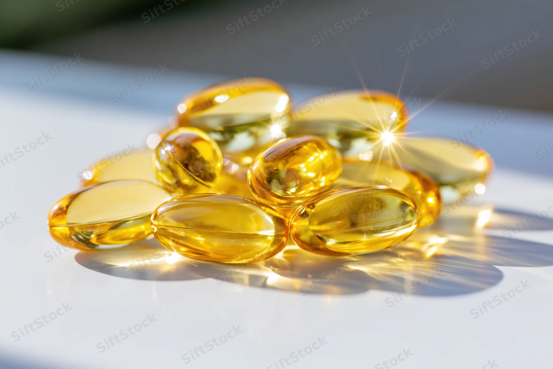 Amber translucent fish oil gel capsules piled on a white surface under bright light