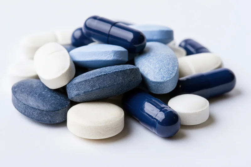 Assorted blue and white pharmaceutical pills and capsules piled on a white surface