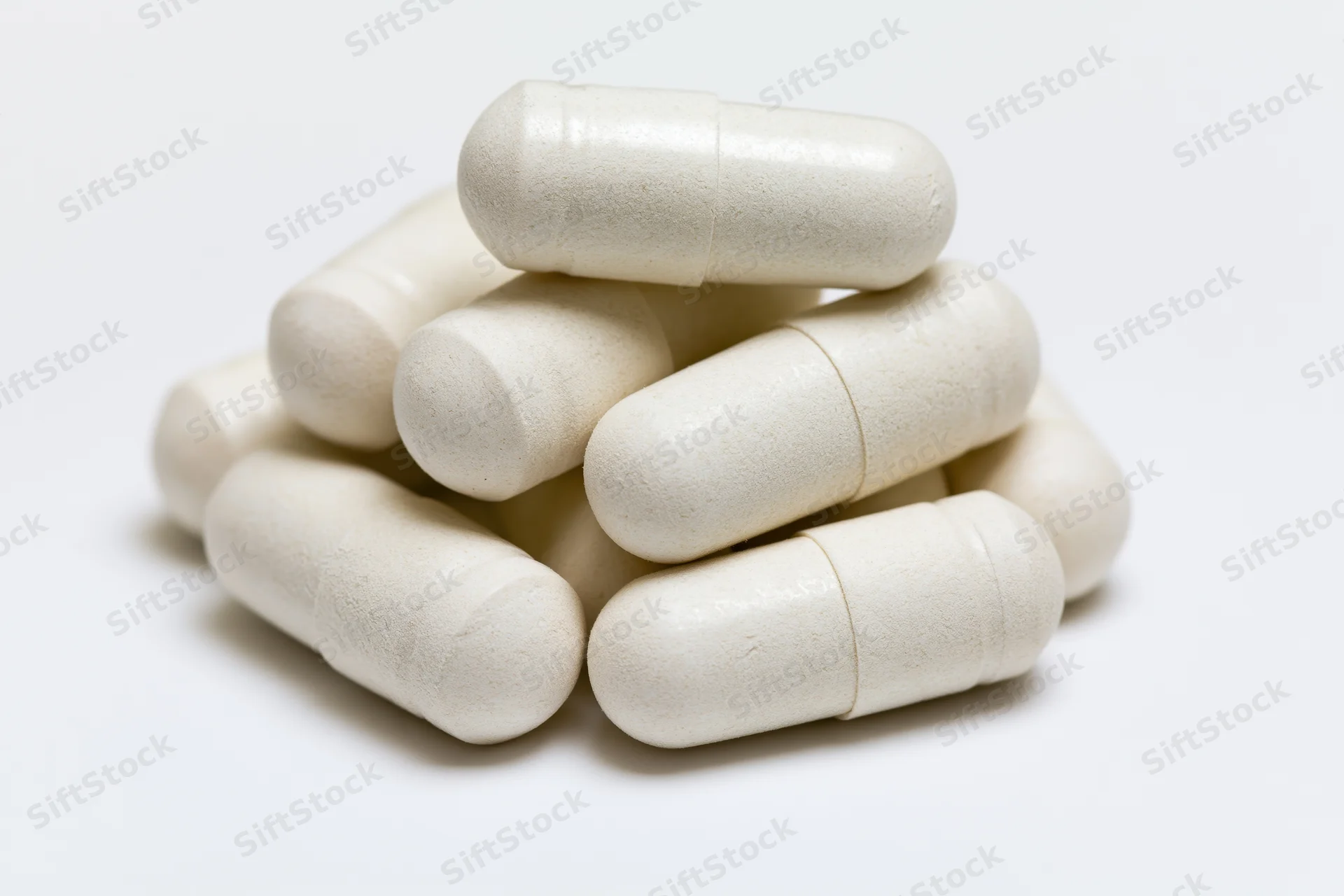 Off-white gelatin supplement capsules stacked in a small pile on a white background