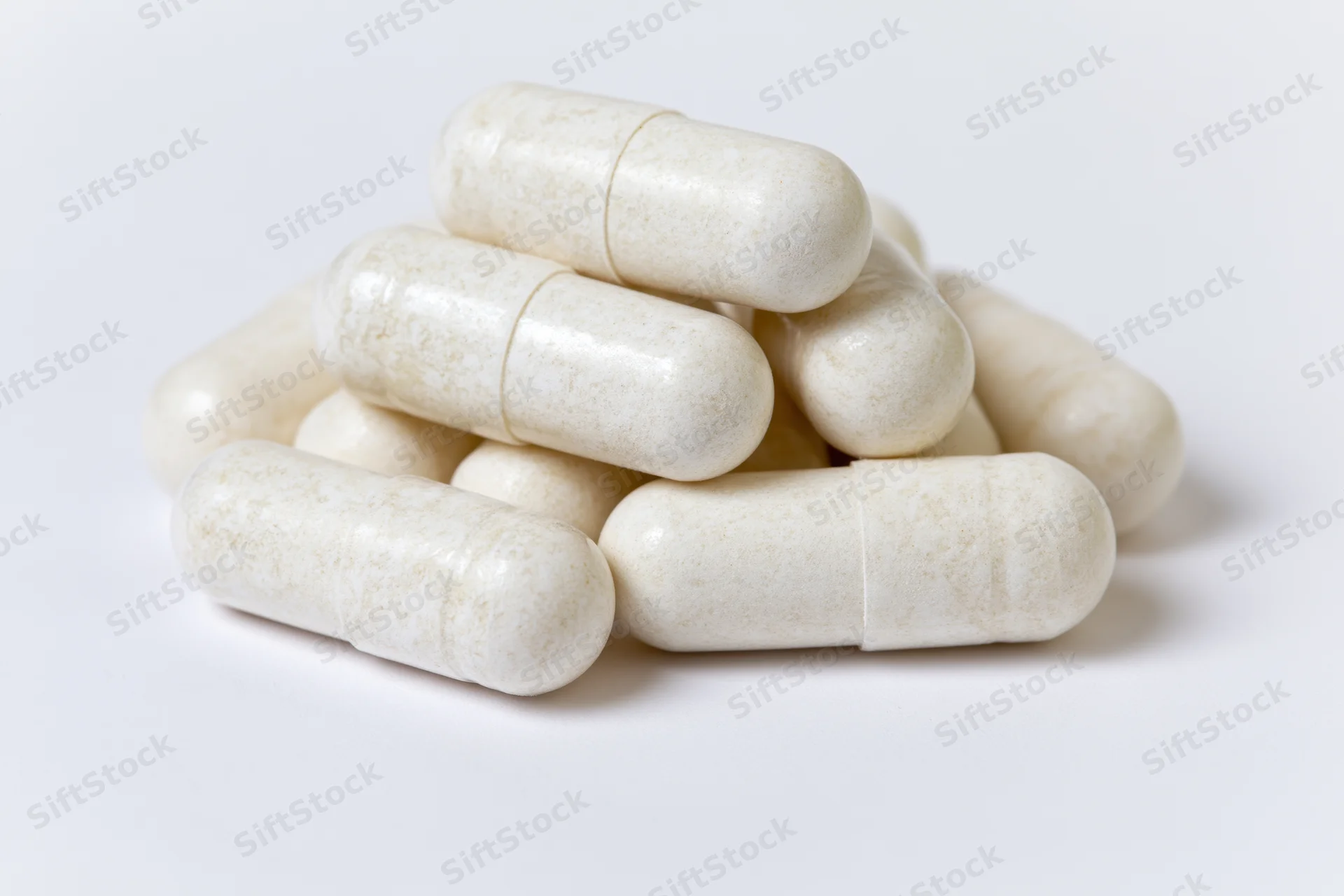 Off-white gelatin supplement capsules stacked in a small pile on a white surface