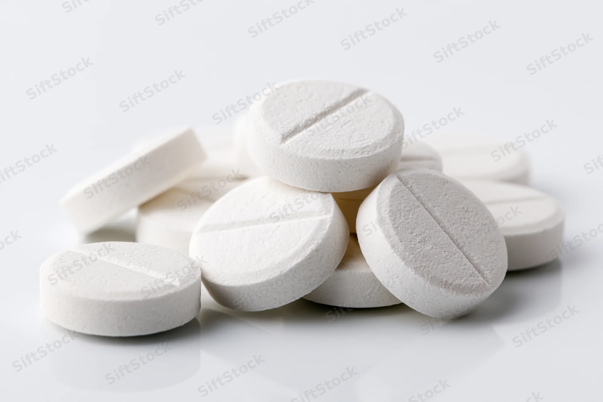 Round white scored tablets scattered loosely on a reflective white surface
