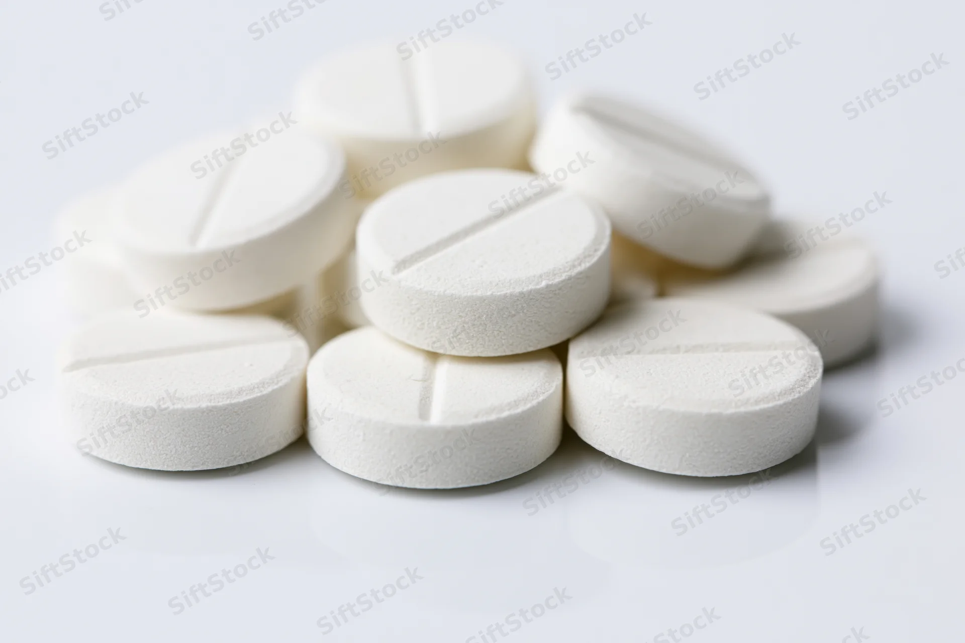 Round white scored tablets piled loosely on a white surface