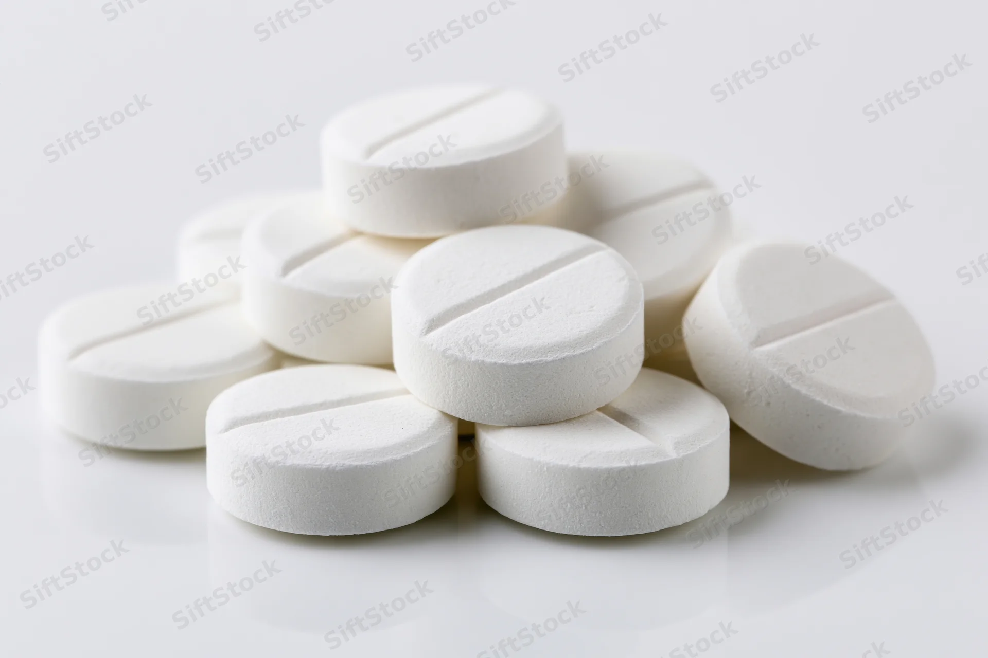 A small pile of round white scored tablets scattered loosely on a white surface