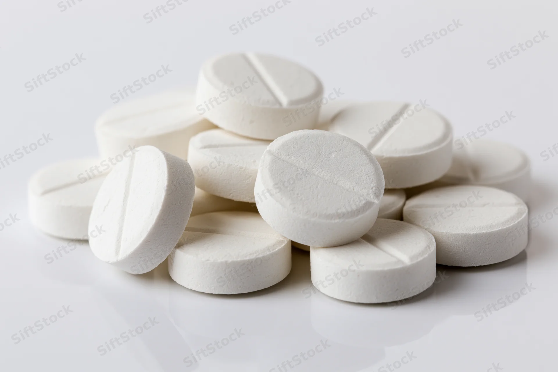 Round white scored tablets piled loosely on a reflective white surface