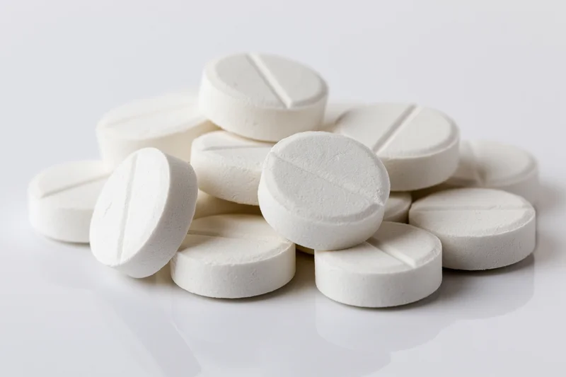 Round white scored tablets piled loosely on a reflective white surface