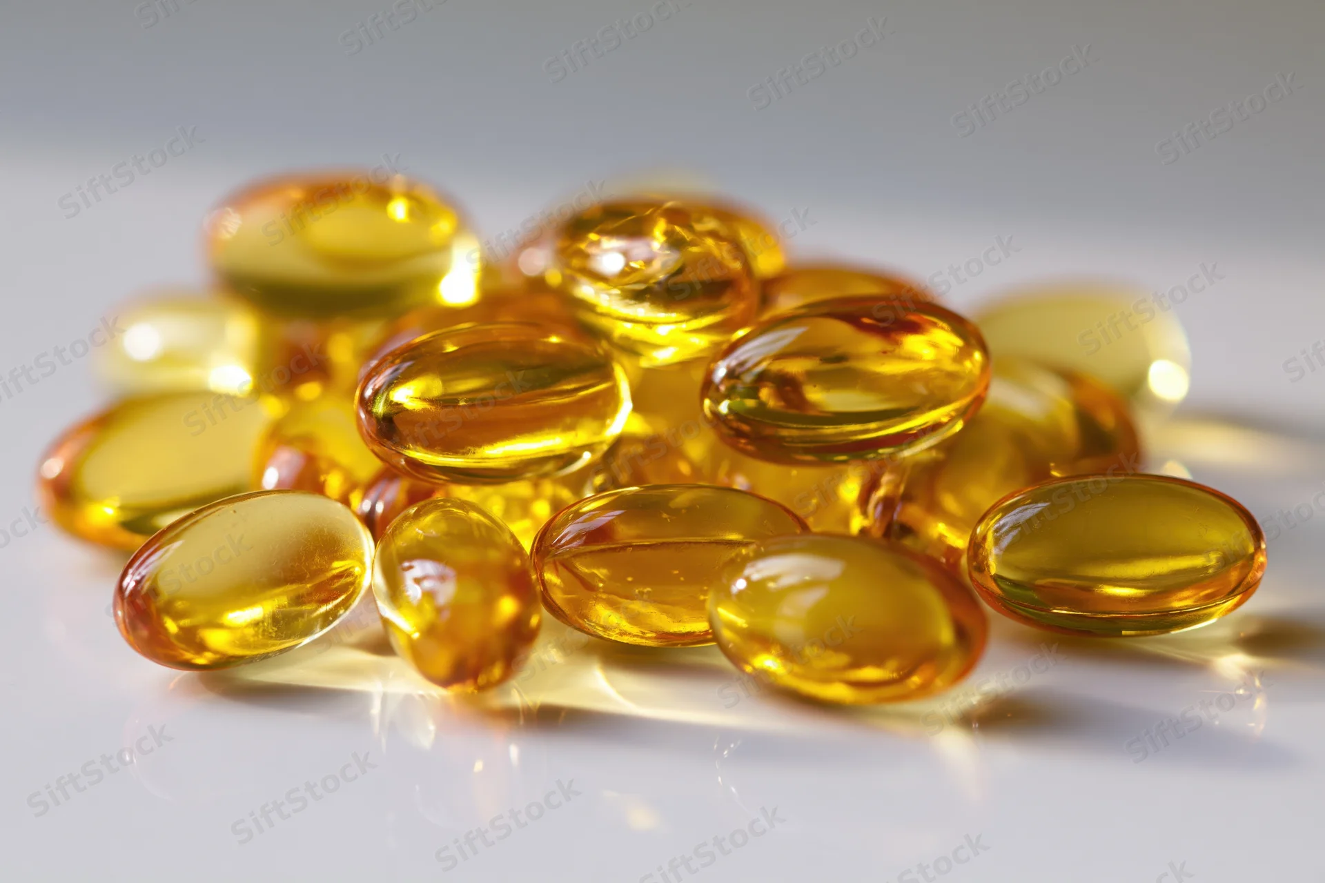 Translucent amber fish oil gel capsules piled on a white reflective surface