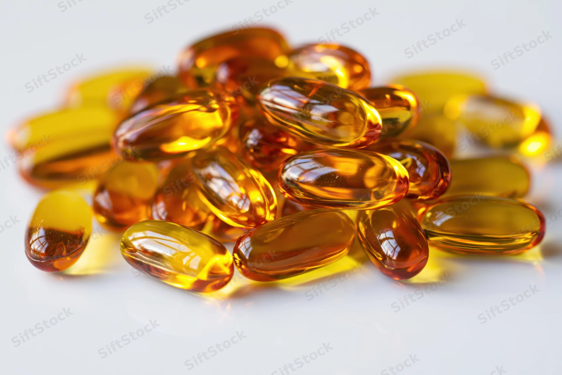 Pile of translucent amber fish oil gel capsules on white surface