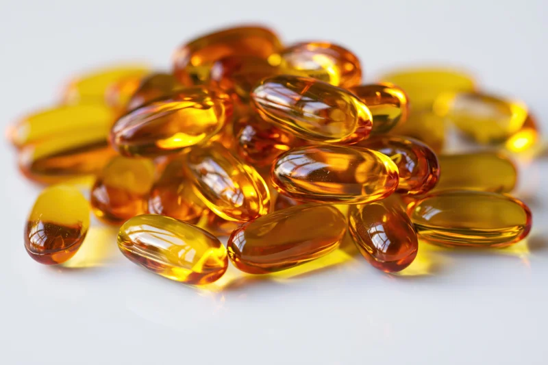 Pile of translucent amber fish oil gel capsules on white surface