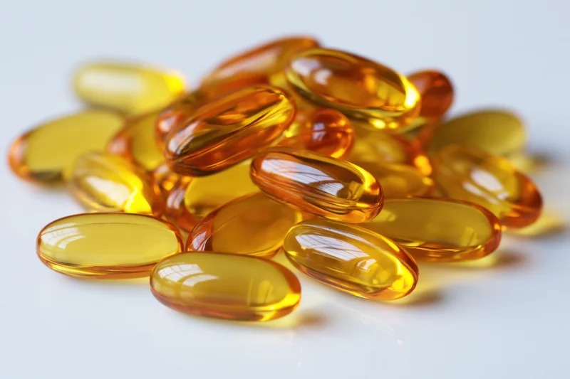 Pile of translucent amber fish oil gel capsules on white surface