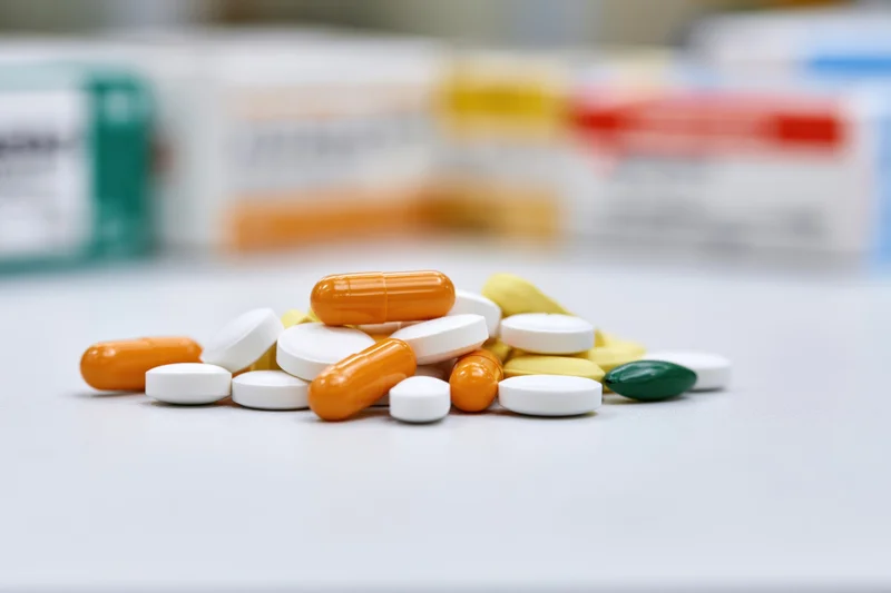 Scattered pile of assorted pills and capsules on a white surface