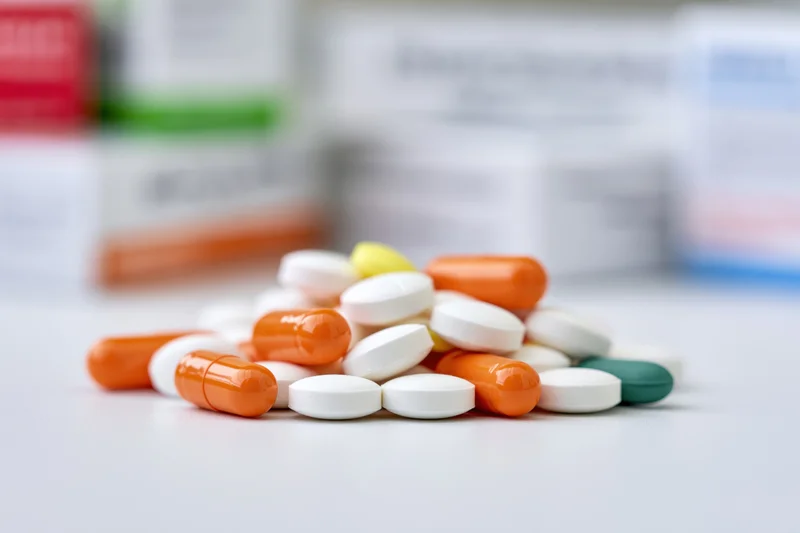 Scattered pills and capsules on a white surface with blurred medication boxes in the background