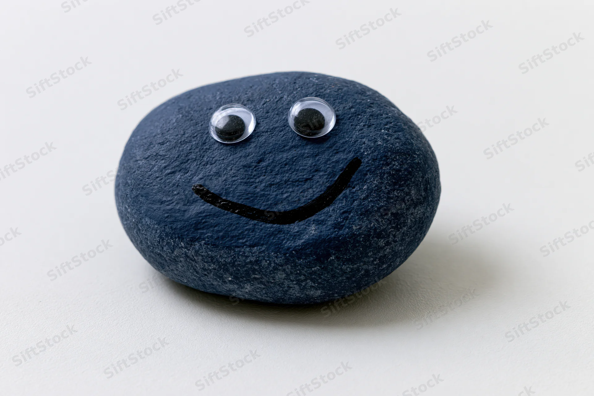 Painted blue rock with googly eyes and smiley face on white background
