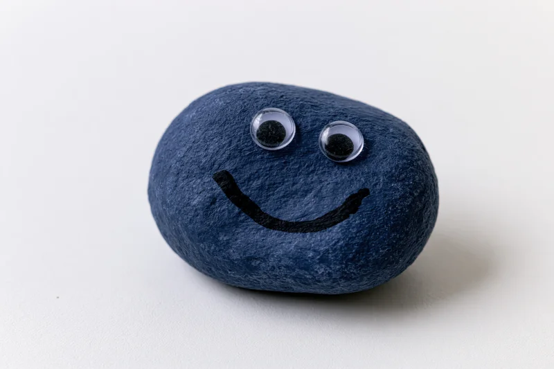 Painted blue rock with googly eyes and smiley face on white background