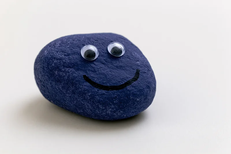 Painted blue rock with googly eyes and smiley face on white background
