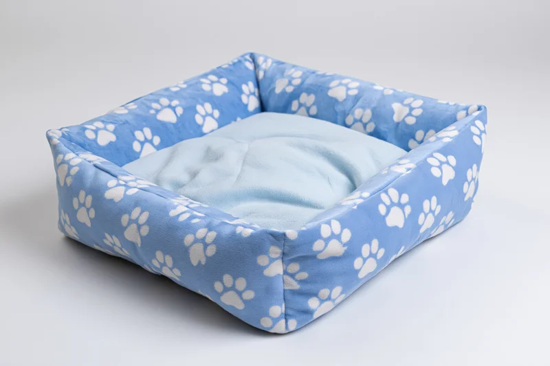 Square pet bed with blue paw print fabric and soft cushion on white surface