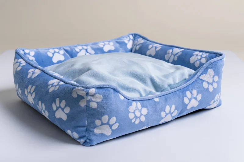 Square blue pet bed with white paw prints on a white surface