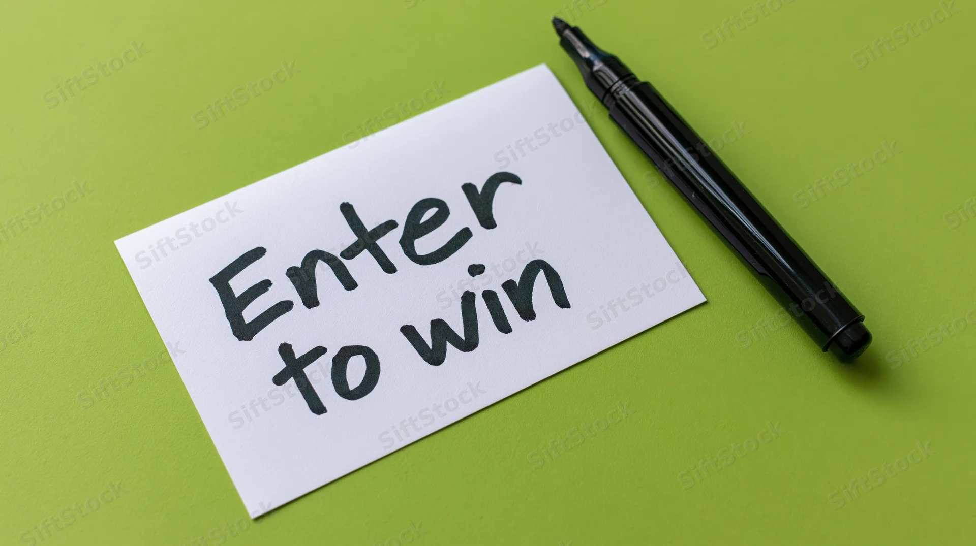 Handwritten note reading enter to win on green surface with black marker beside it