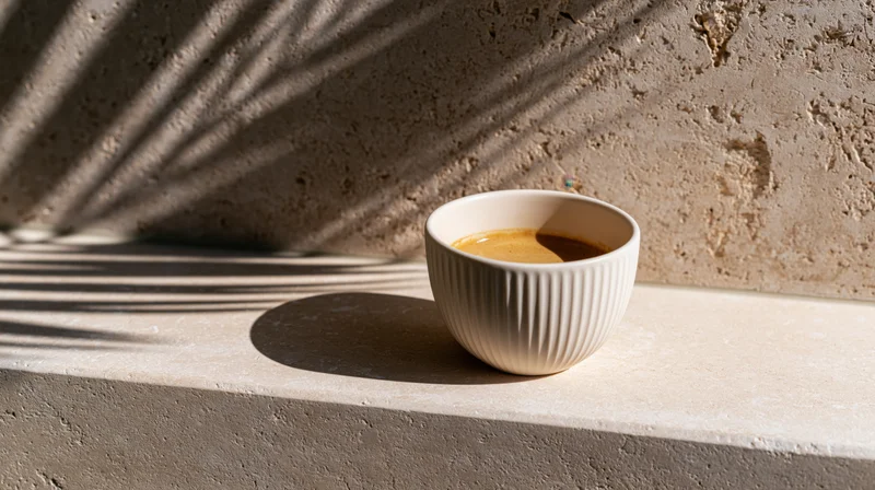 White ridged ceramic cup filled with espresso on a concrete ledge with leaf shadows in natural sunlight