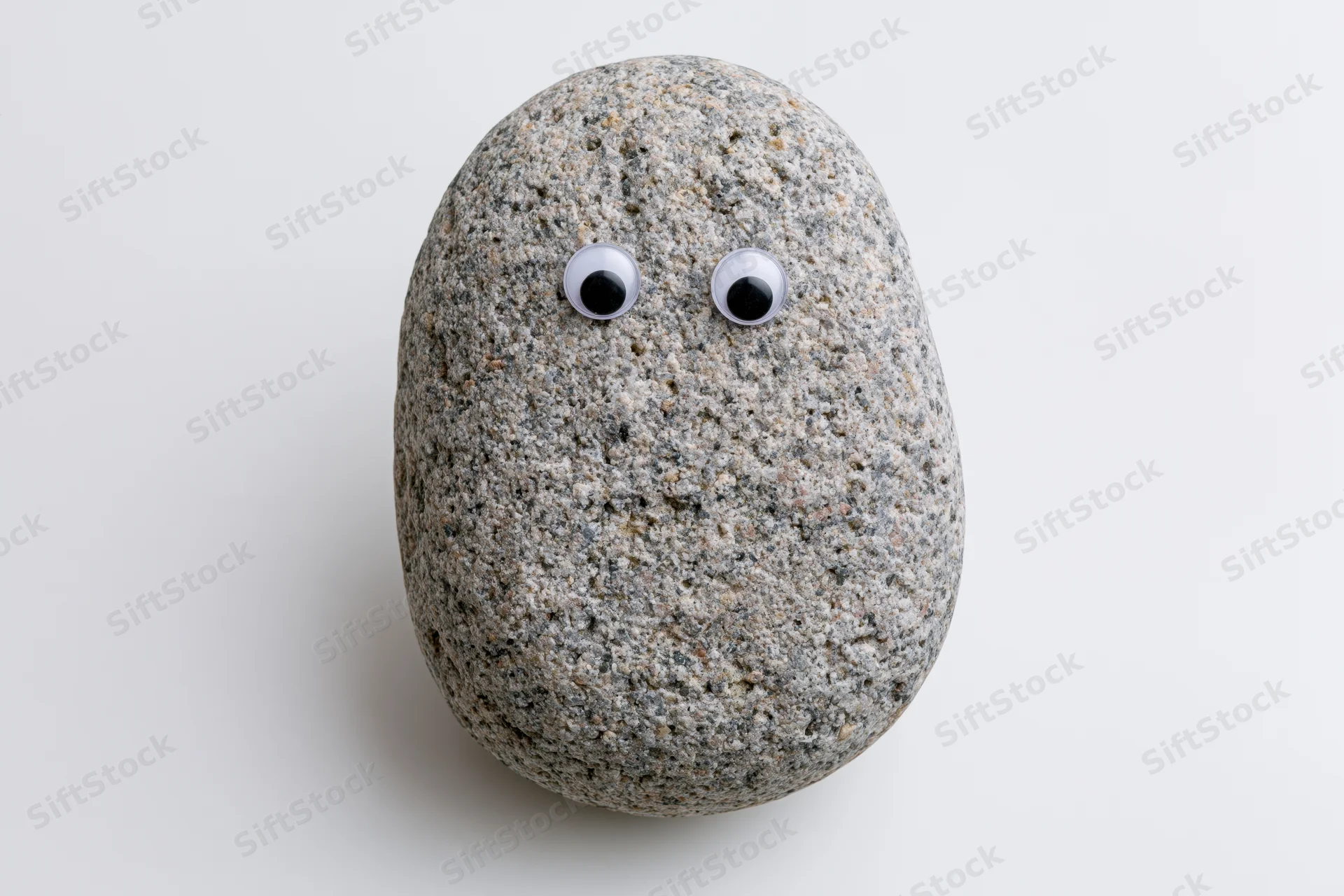 Smooth grey river rock with googly eyes on white background
