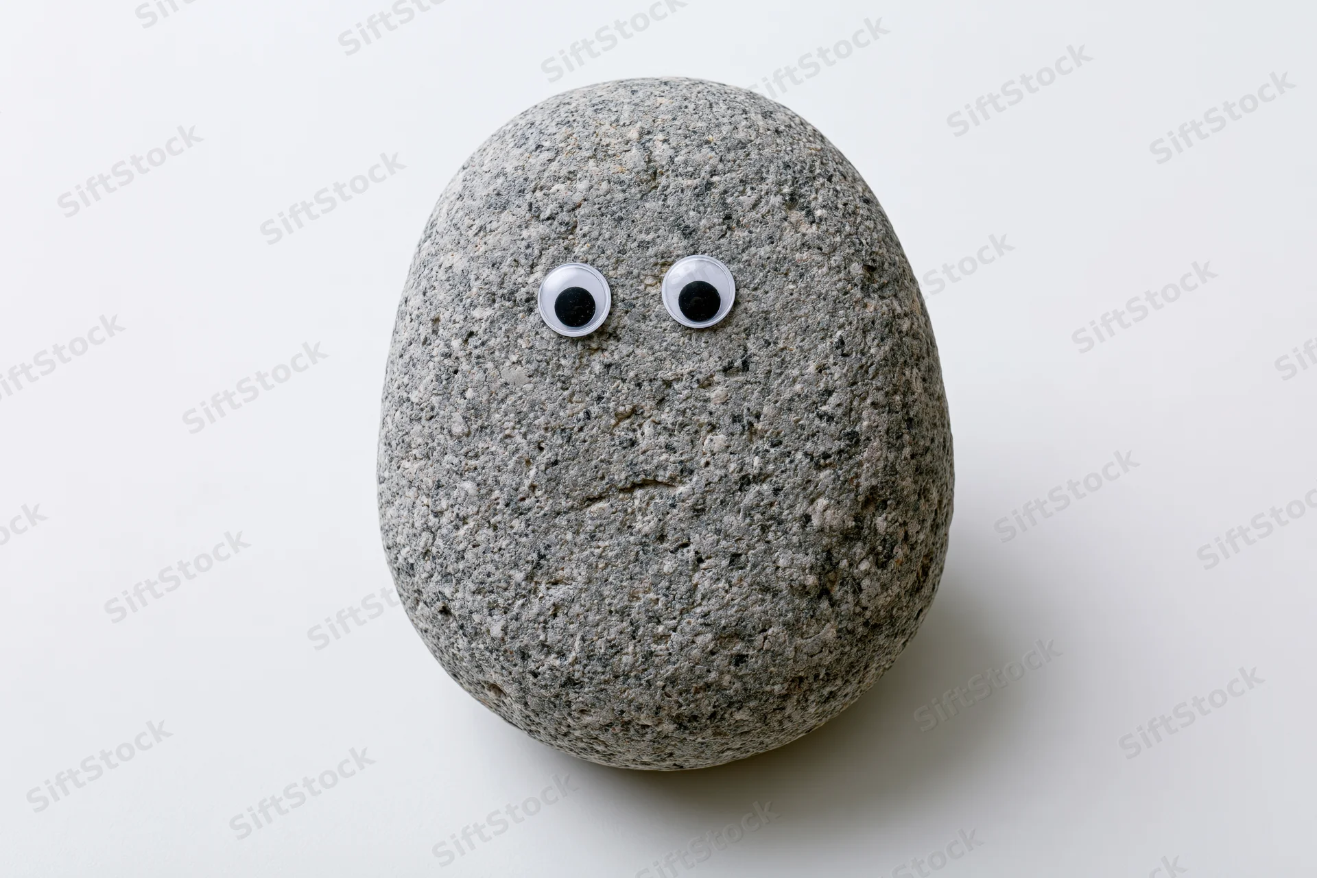 Smooth grey river rock with googly eyes on white surface