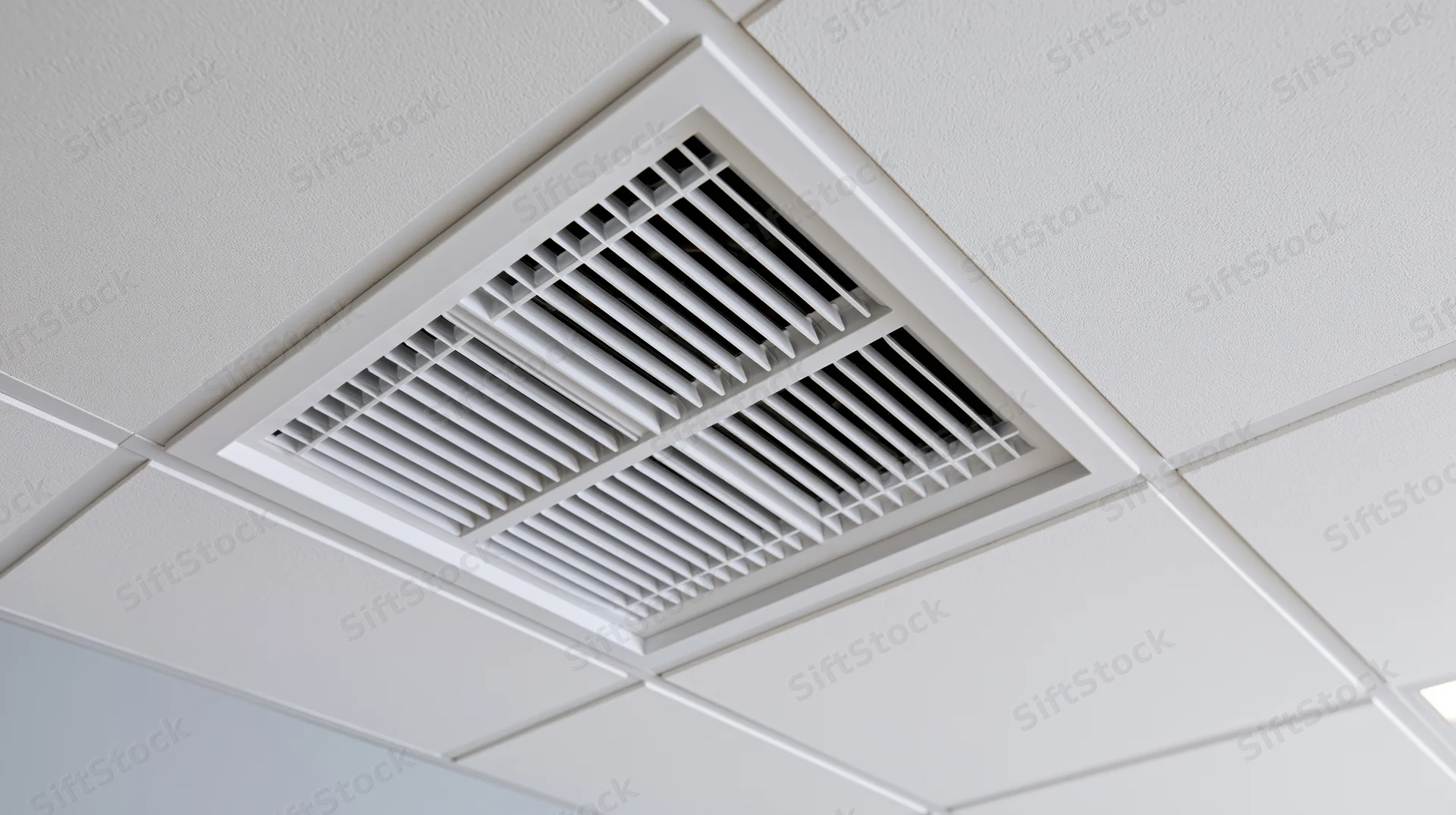 White square hvac diffuser mounted flush in a ceiling tile grid