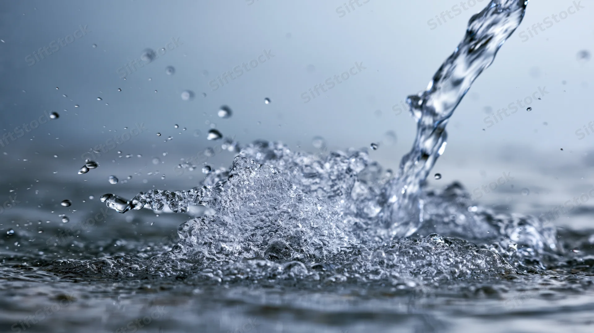 Stream of water splashing onto wet surface creating droplets and ripples
